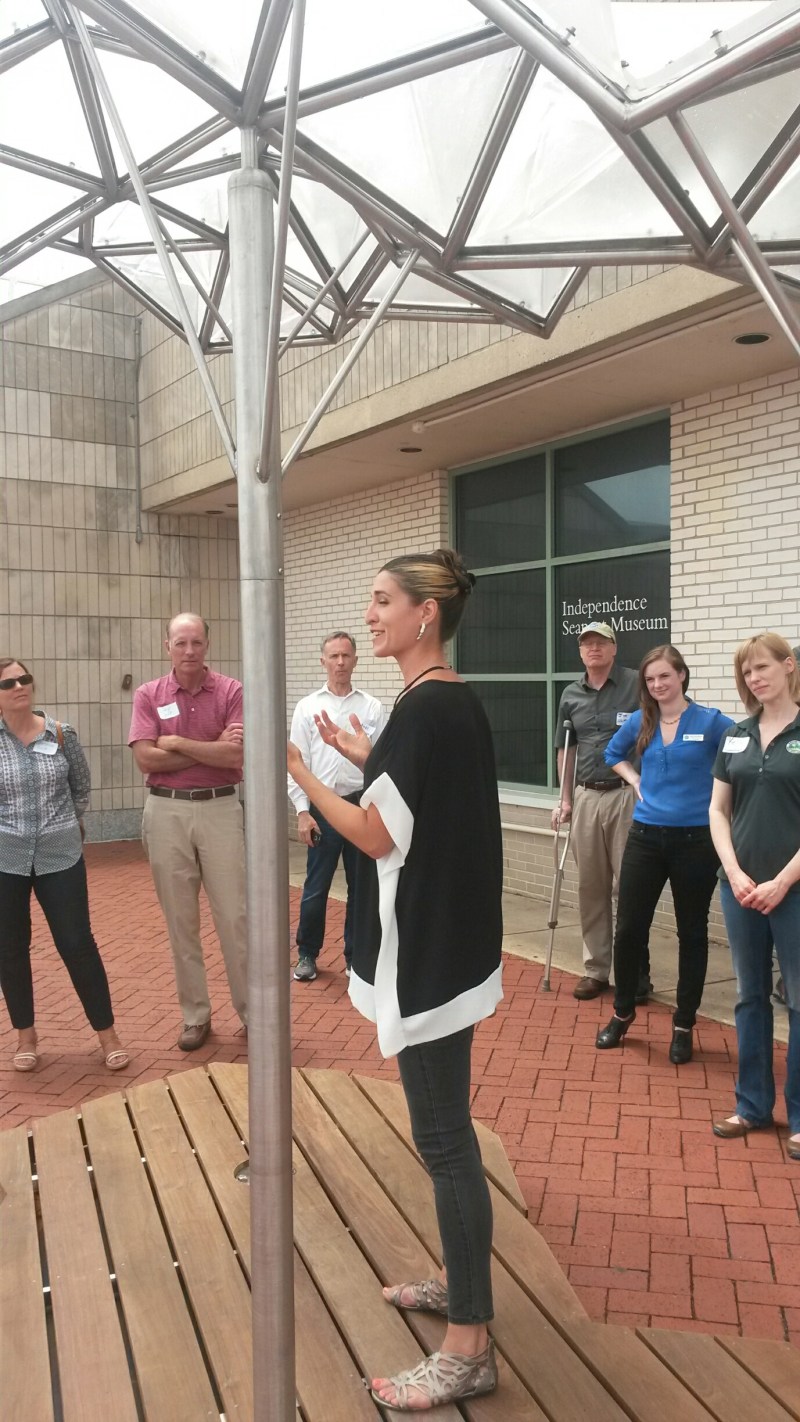 Alison Stigora standing under the canopy of Hydraulica speaking to guests at the exhibit opening